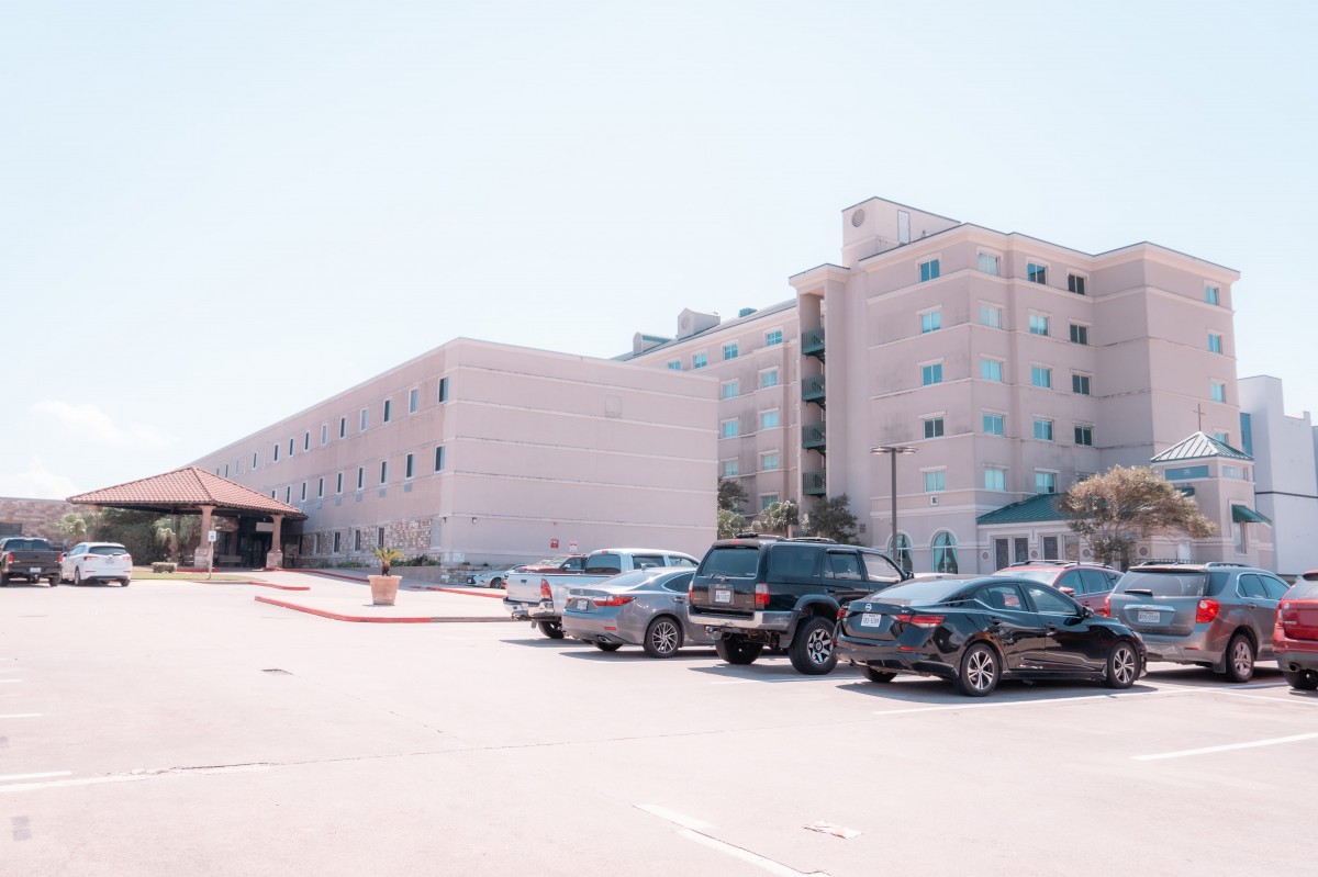 A parking lot in front of a large multi-story building on a clear day.