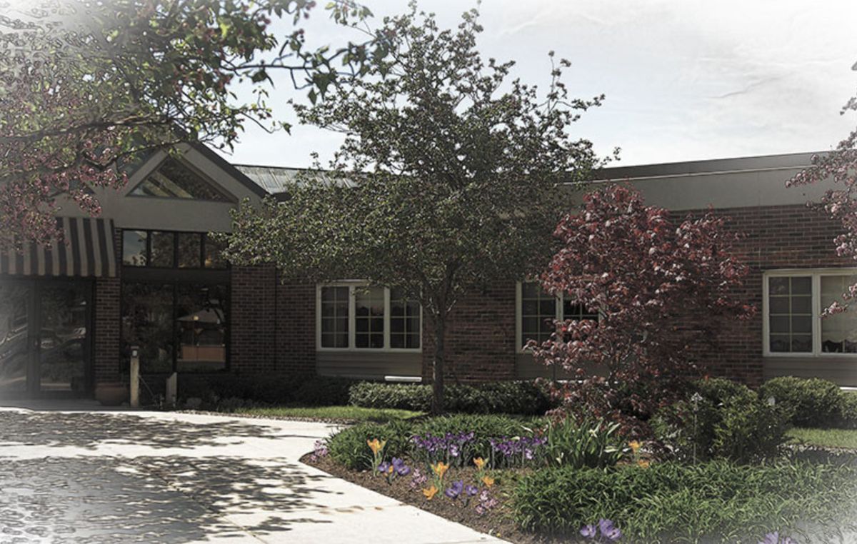A view of a building surrounded by trees and flowers with a pathway leading to the entrance.