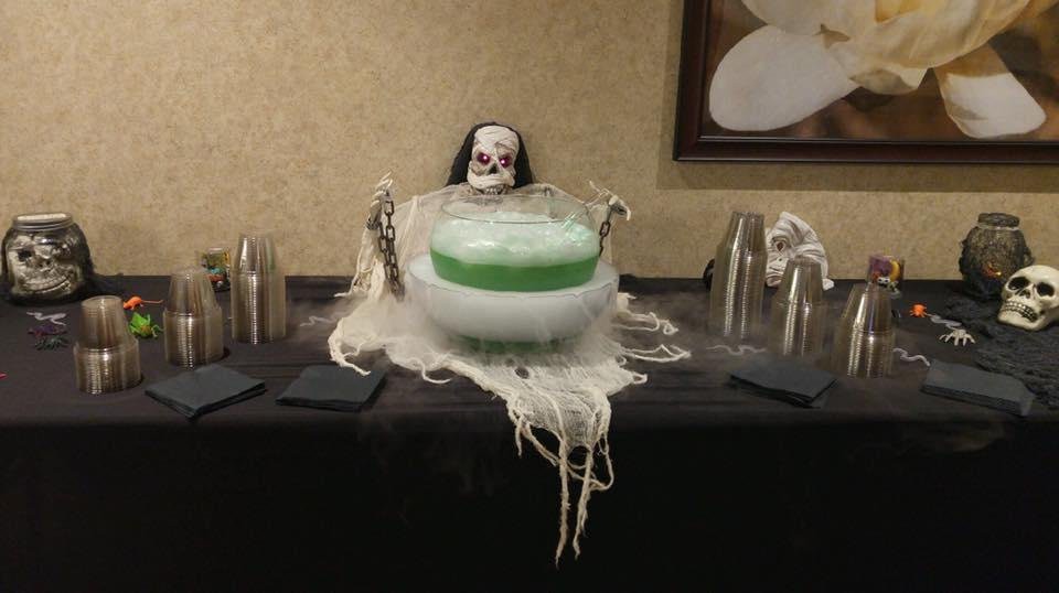 A spooky Halloween punch table featuring a skeleton decoration and a bubbling green drink.