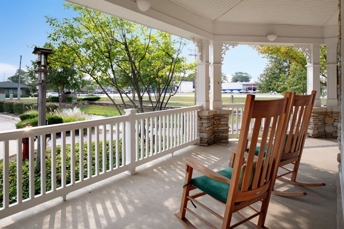A cozy porch with a wooden rocking chair overlooking a sunny front yard.