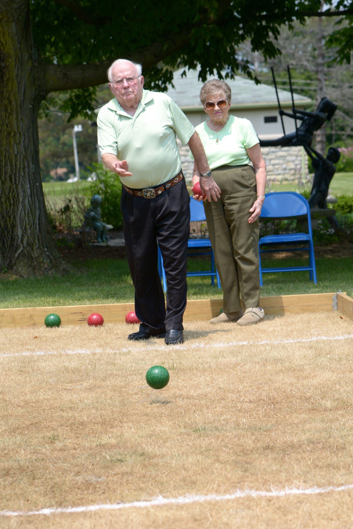 Elderly individuals playing bocce ball outdoors in a park.