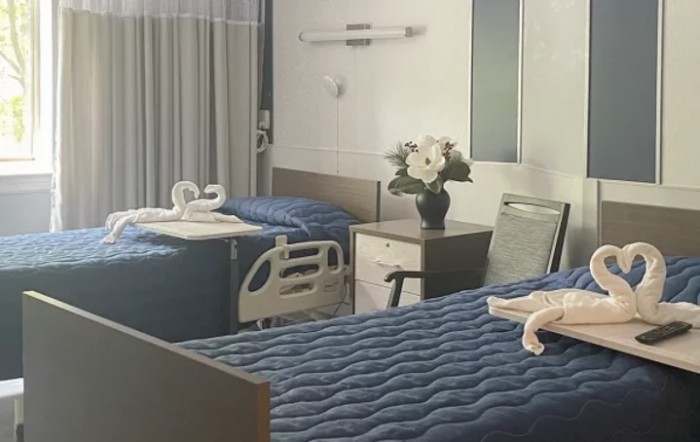 A hospital room with two beds, neatly arranged with flowers on a bedside table.