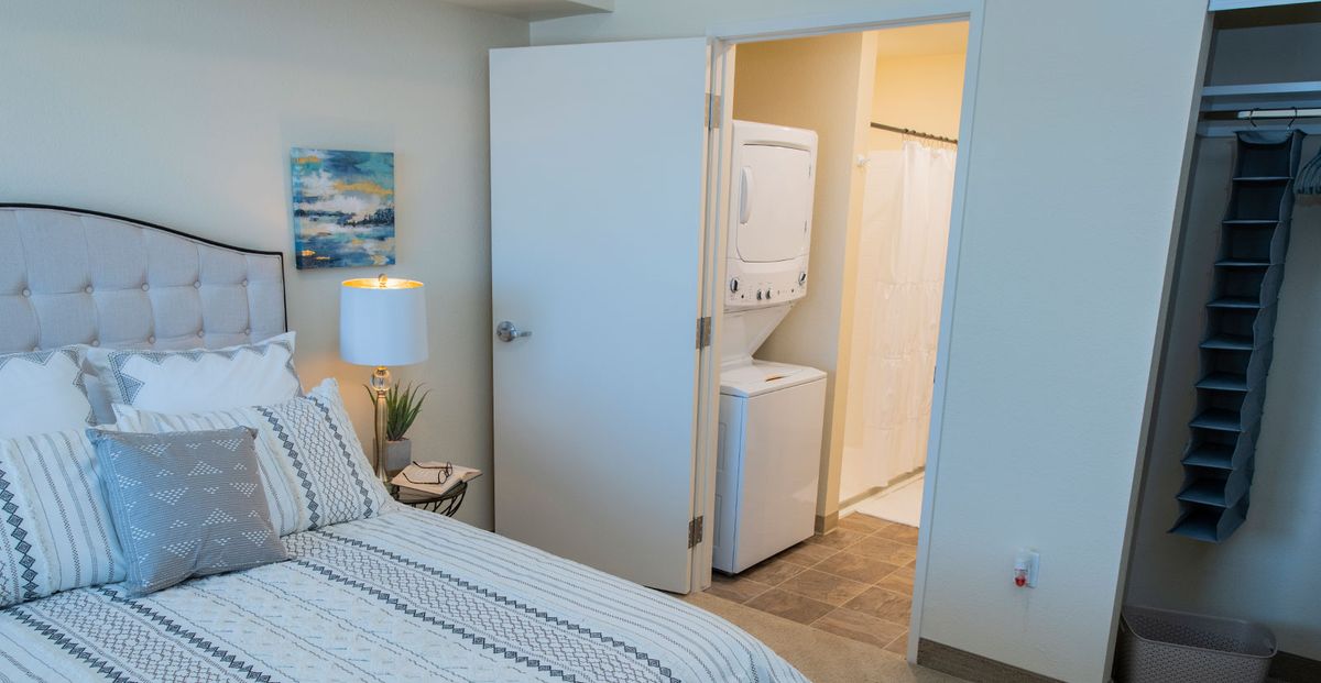 A cozy bedroom with a laundry area featuring a stacked washer and dryer unit.