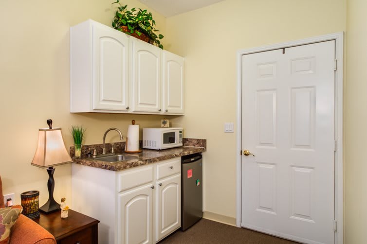 A small kitchen area with white cabinets, a microwave, and a mini fridge.