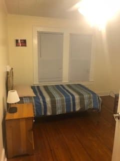 A minimalist bedroom with a bed, nightstand, and lamp next to two large windows.