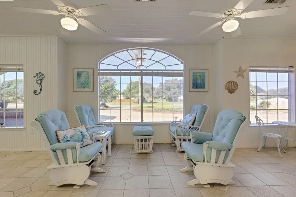A cozy seating area with several light blue chairs arranged around a large window, illuminated by overhead ceiling fans.
