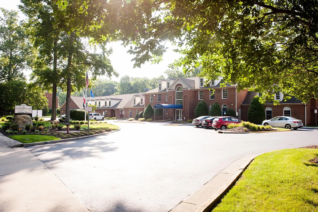 A sunny day at a brick building with a parking lot surrounded by trees.