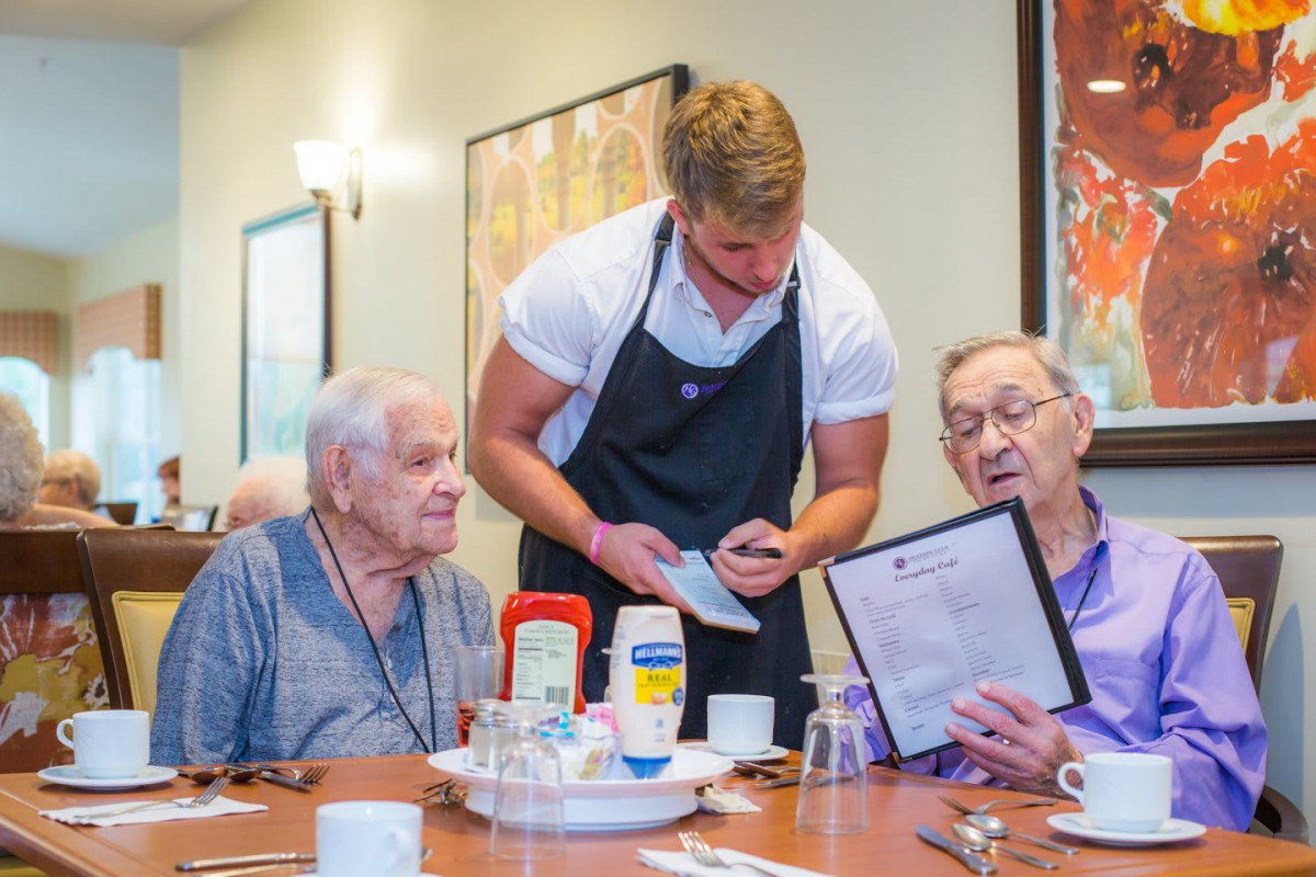 A waiter taking an order from two elderly customers at a restaurant.