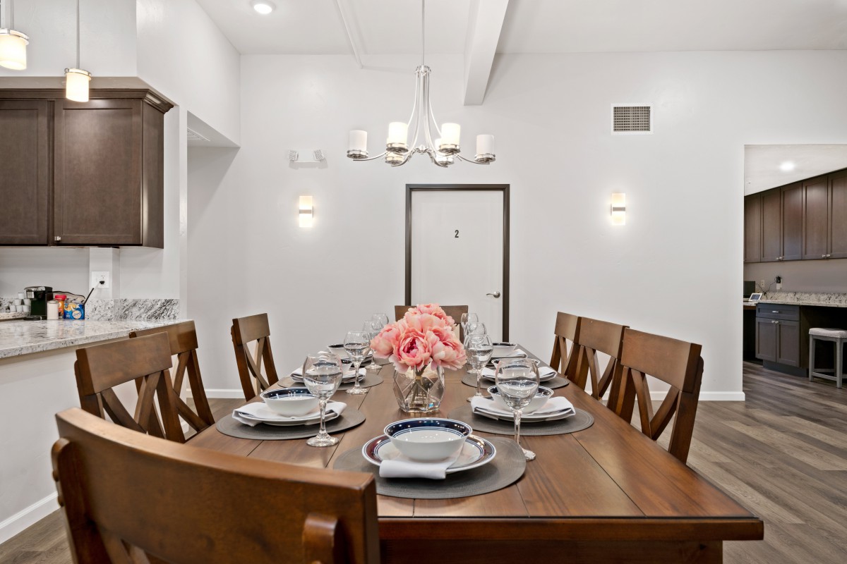 A beautifully set dining table with wooden chairs, elegant dinnerware, and a floral centerpiece under a modern chandelier.