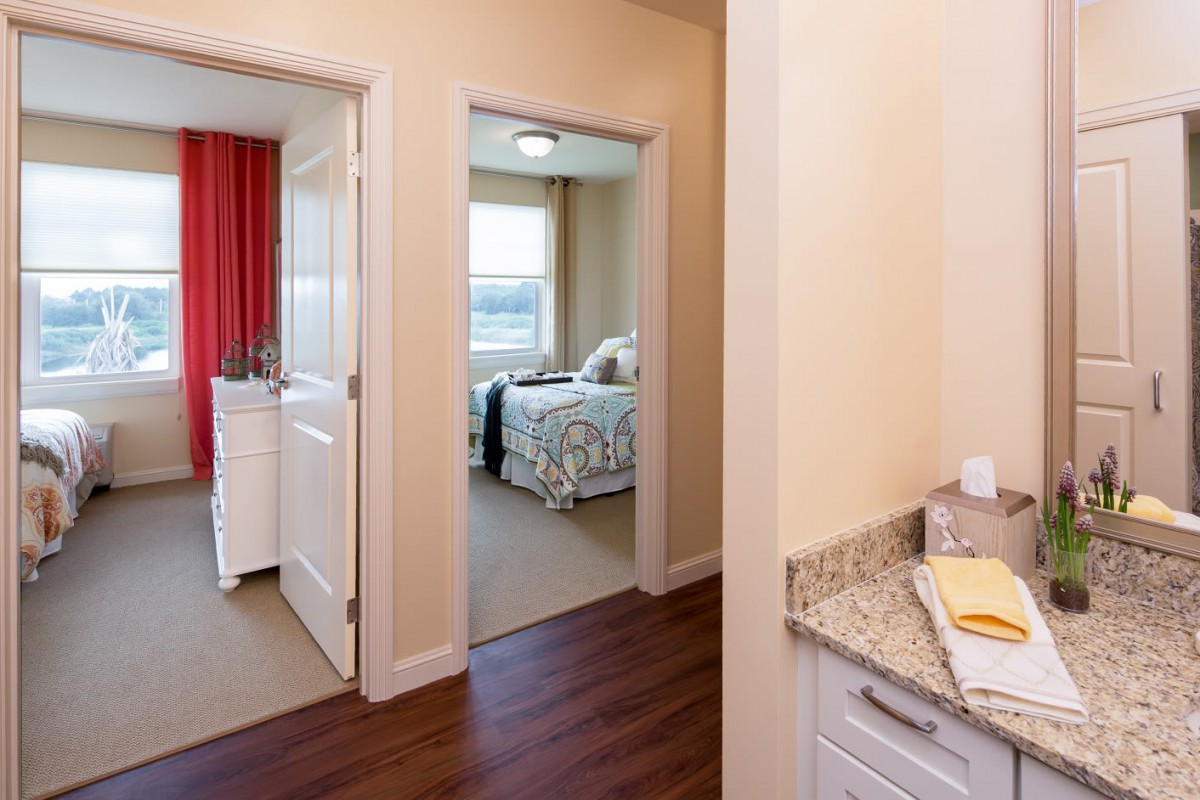 A view of a hallway leading to two bedrooms in a modern apartment.