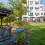 A serene garden with a gazebo, vibrant hydrangeas, and a building in the background with red patio umbrellas.