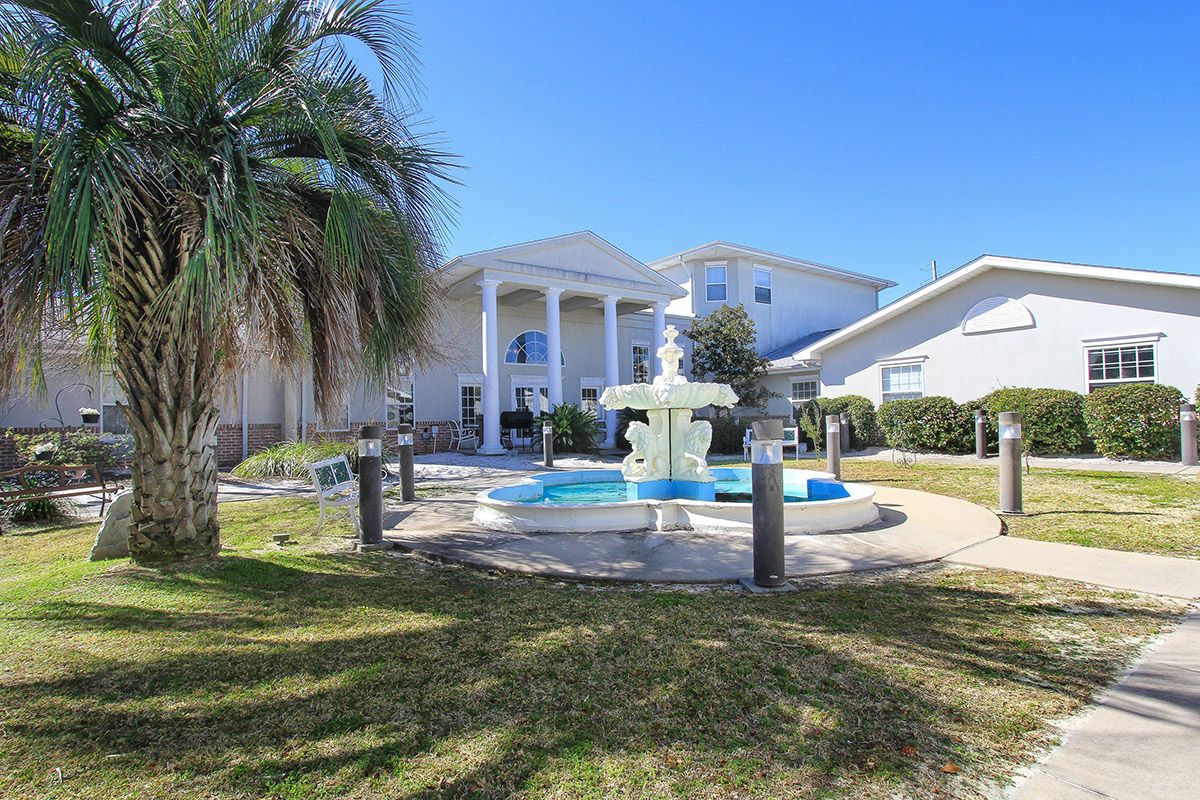 A beautiful house with a fountain in the front yard, surrounded by a manicured lawn and palm tree under a clear blue sky.
