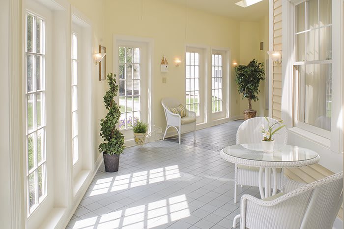 A bright sunroom with white furniture and large windows.