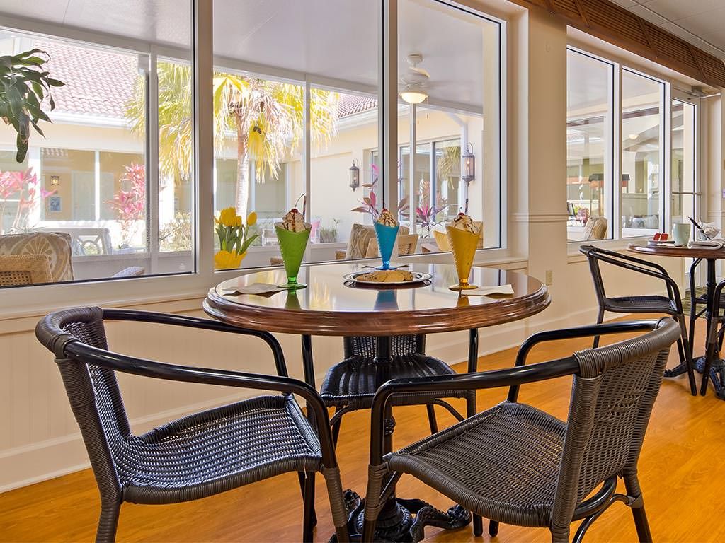 A cozy dining area with a round glass table surrounded by wicker chairs, adorned with colorful decorative plants under abundant natural light.