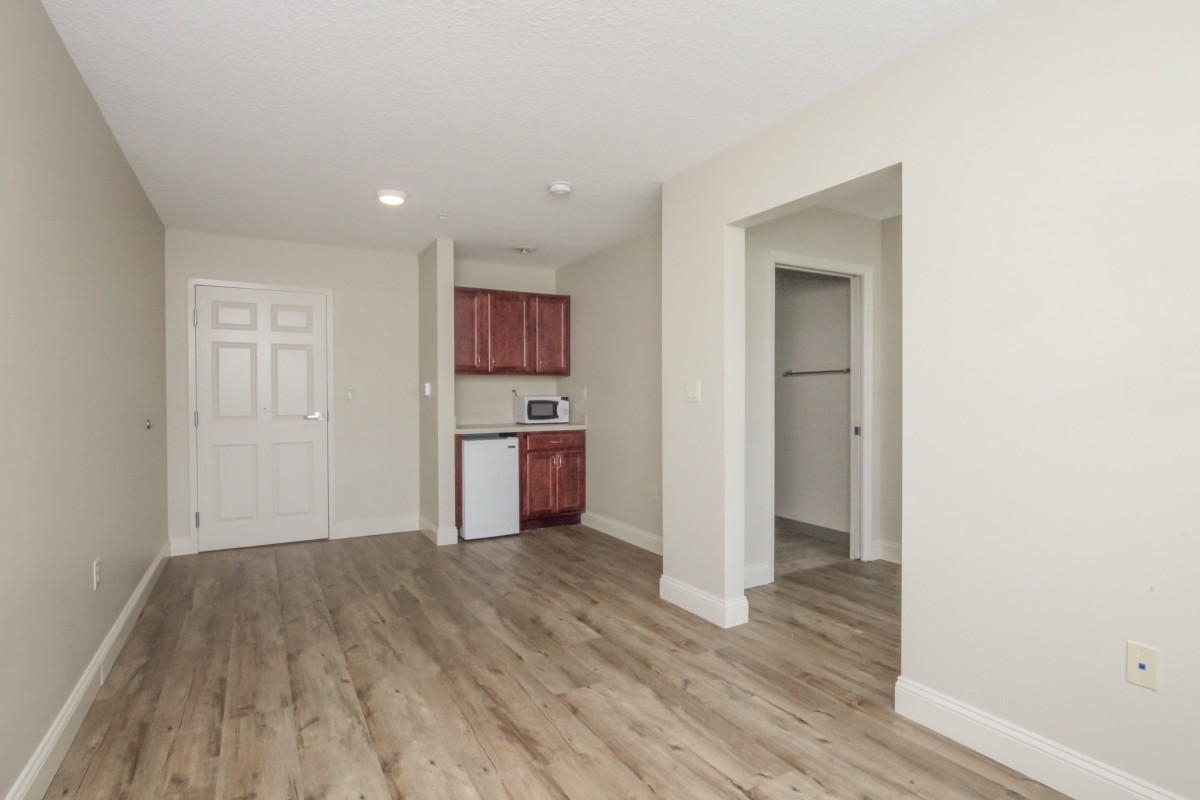 An empty apartment interior featuring a kitchenette and wood flooring.