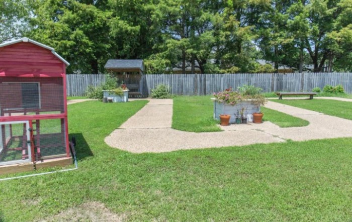 A well-maintained backyard with a grassy lawn, pathways, and planters, surrounded by a wooden fence and trees.