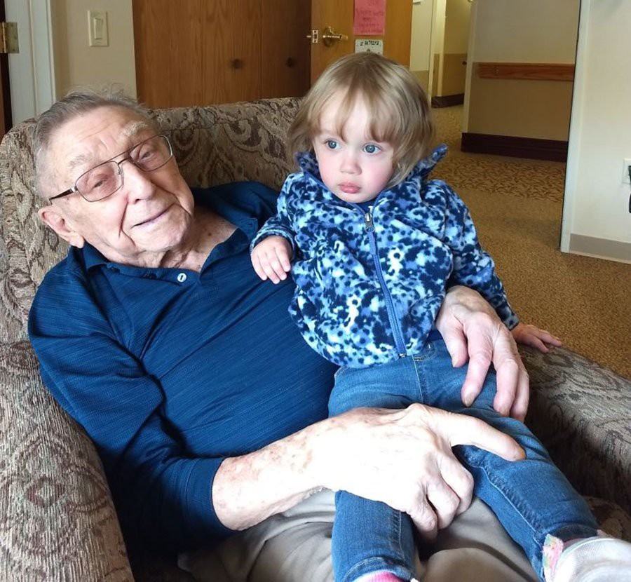 An elderly man sitting on a couch, holding a toddler on his lap.