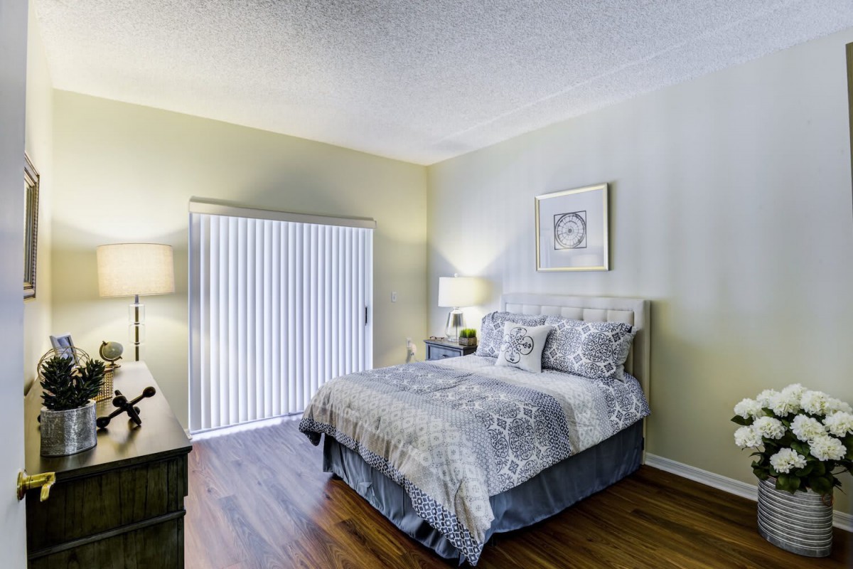 A cozy bedroom featuring a neatly made bed with patterned bedding, two bedside lamps, and hardwood flooring.