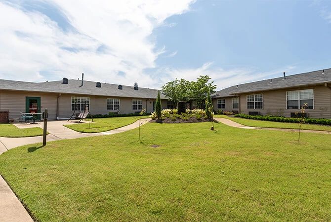 A residential apartment complex with a central courtyard featuring a well-maintained lawn and pathways.