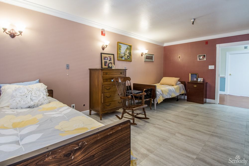 A cozy bedroom with two single beds, a wooden dresser, and a rocking chair, adorned with paintings on the walls.