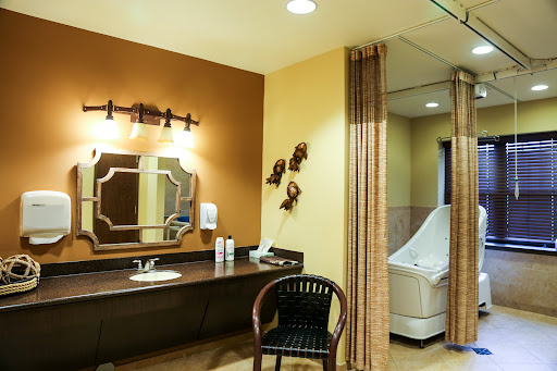 A spacious and well-lit bathroom featuring a vanity area, mirror, and comfortable chair.