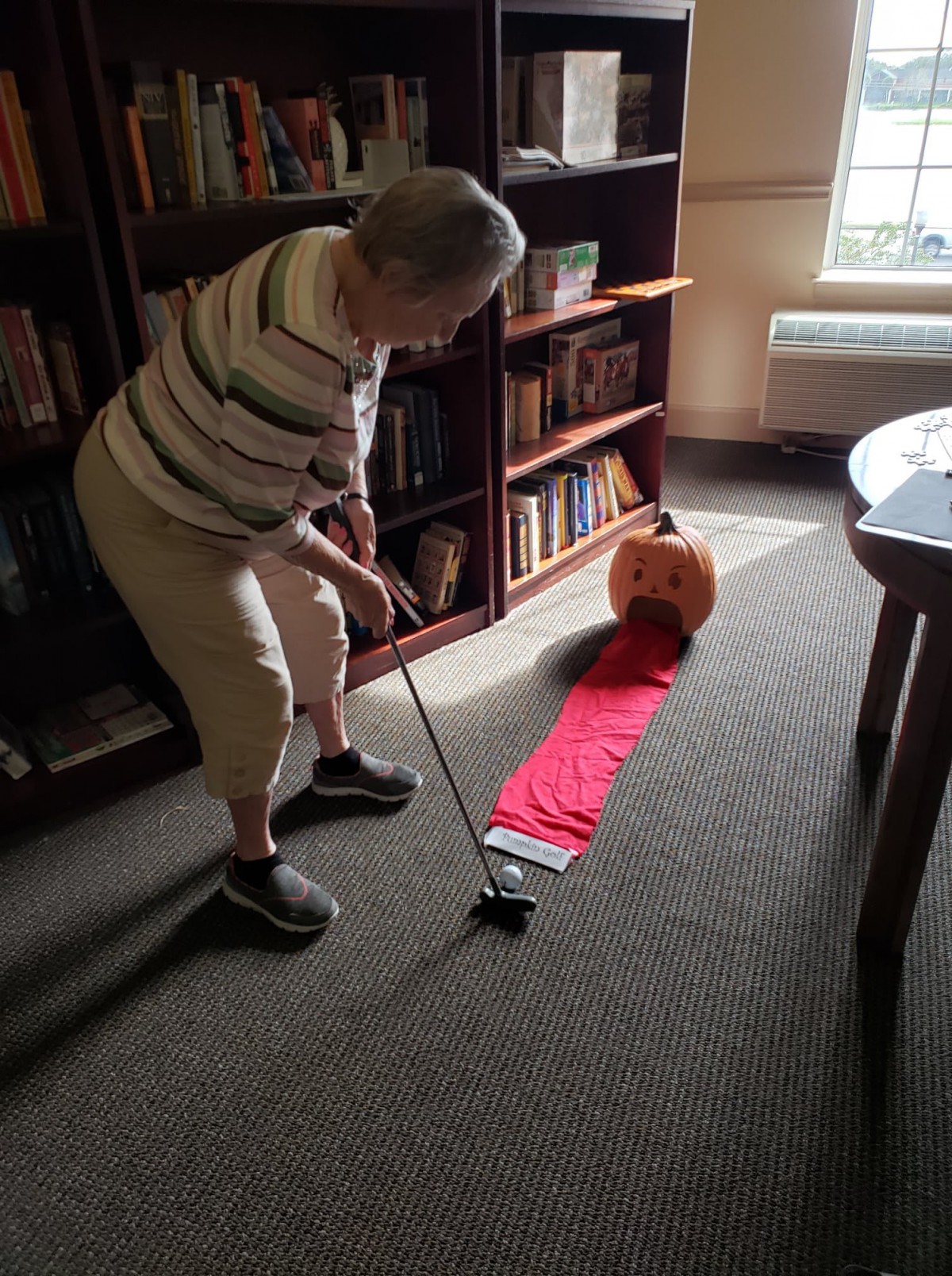 An elderly person playing indoor mini-golf with a pumpkin target.