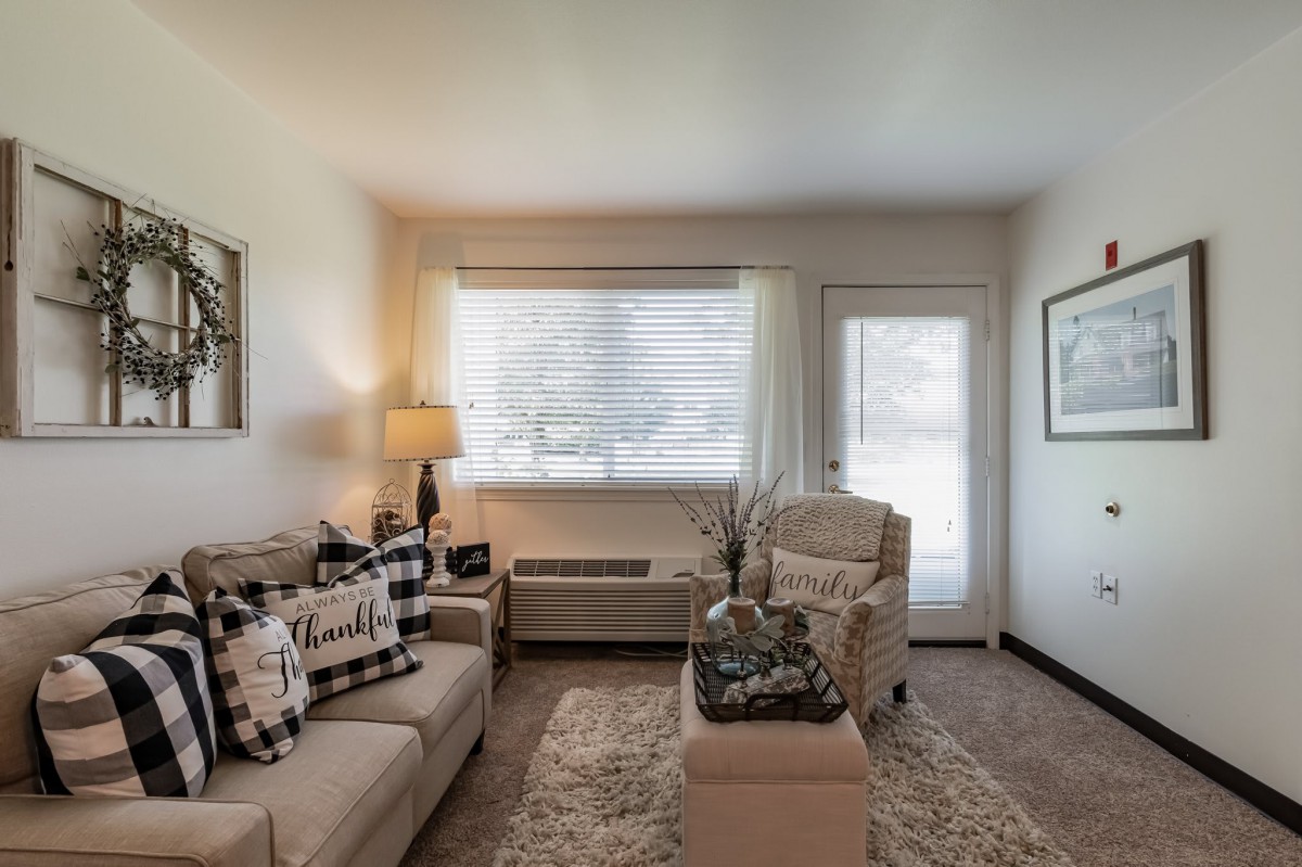 A cozy living room with comfortable seating, a lamp, and ample natural light from the window.
