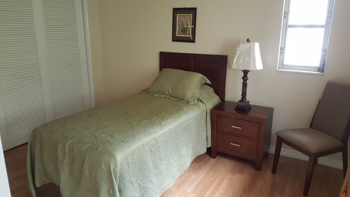 A simple bedroom with a single bed, nightstand, and lamp.