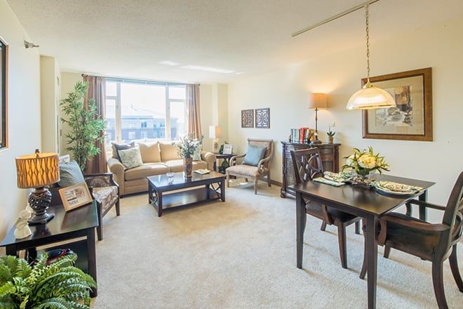 A cozy living room with a comfortable sofa, coffee table, and adjacent dining area, well-lit by natural sunlight.