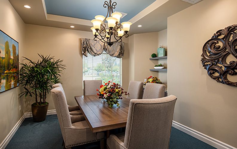 A beautifully decorated dining room featuring a wooden table, upholstered chairs, a decorative chandelier, and natural light from a window.