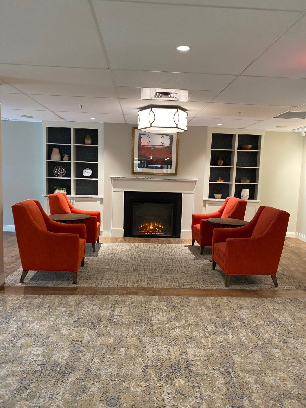 A cozy seating area with a fireplace, featuring four red chairs arranged around a central hearth.