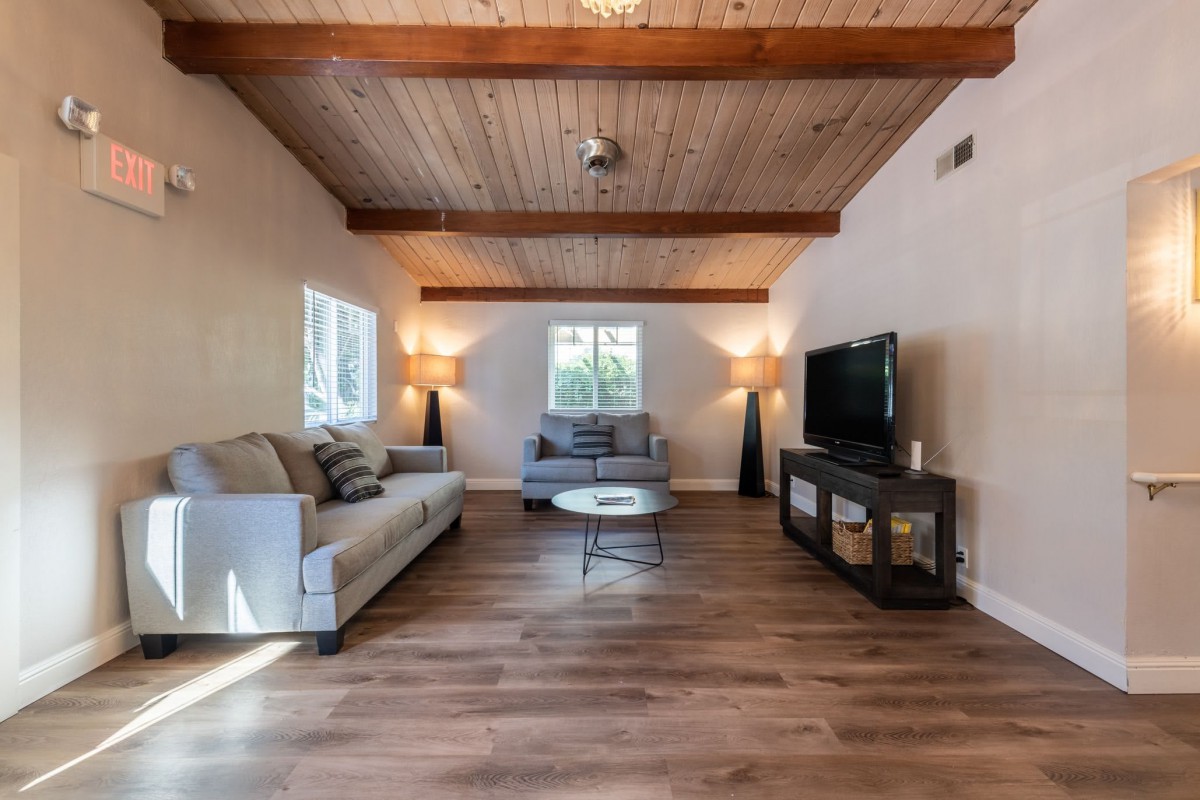 A cozy living room with wooden ceilings, two sofas, a coffee table, and a TV on a stand.