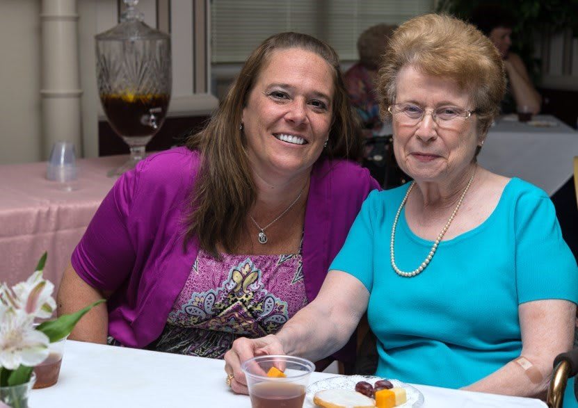 Two women smiling and sitting at a table during an indoor event.