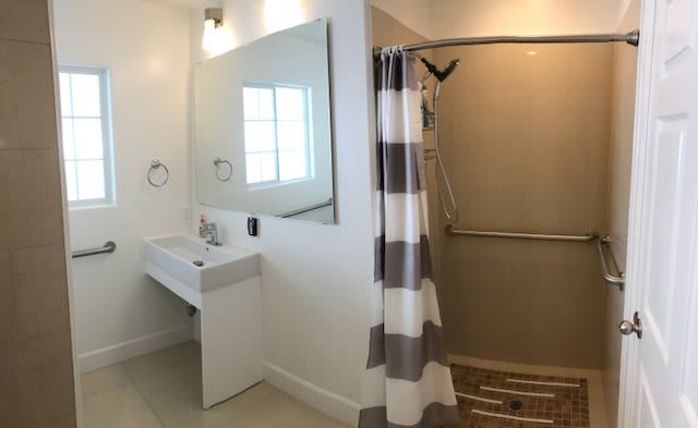 A modern bathroom with a walk-in shower, striped shower curtain, and a sleek sink with a mirror above.
