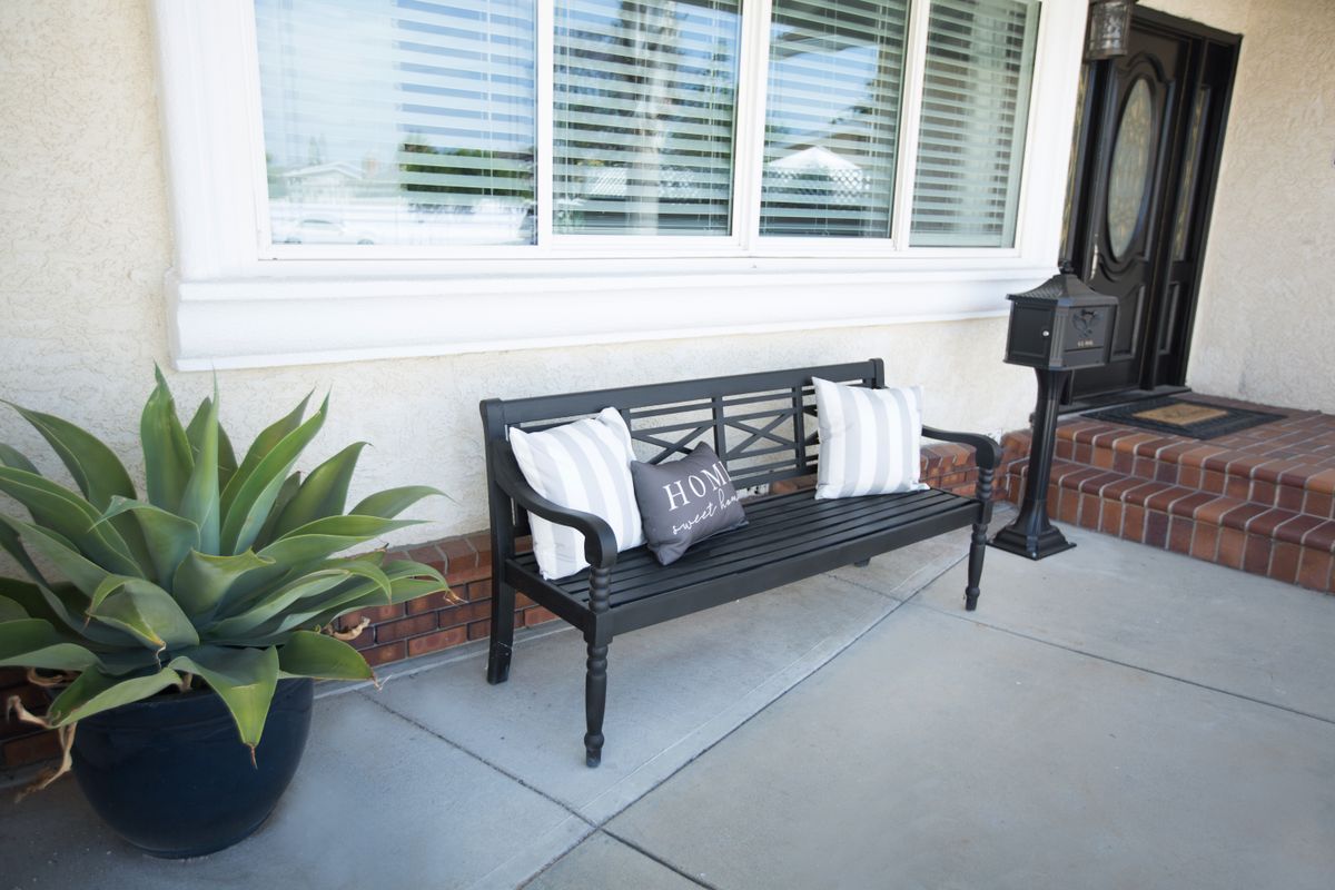 An inviting outdoor bench with decorative pillows, positioned under a large window on a patio.