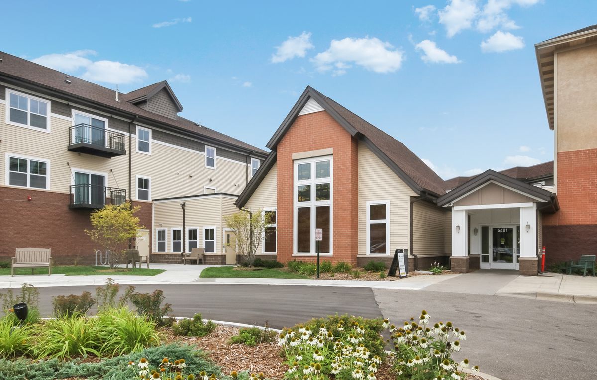 A modern residential building with a landscaped entrance and large windows.
