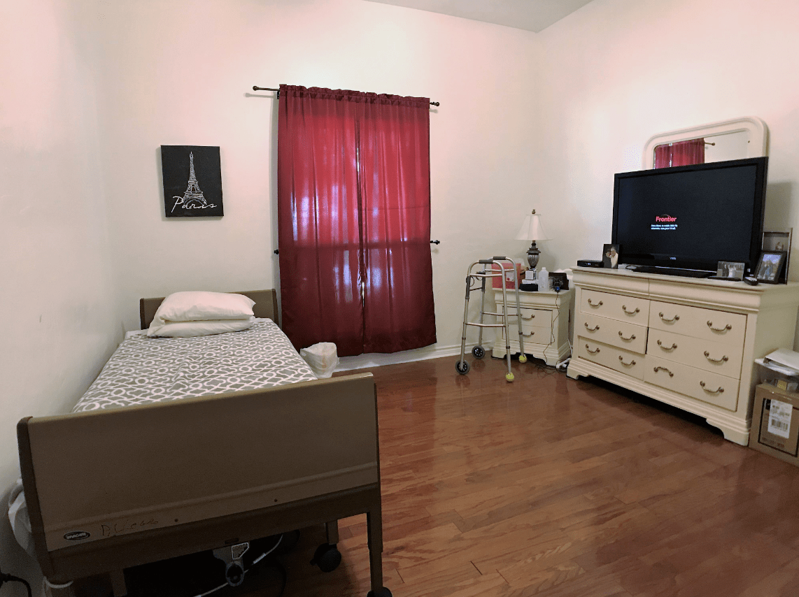 A bedroom with a hospital bed, dresser, TV, and red curtains.