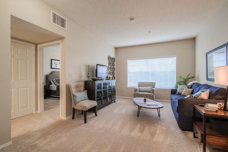 A cozy living room with modern decor, featuring a sofa, chairs, coffee table, and a television in front of a large window.