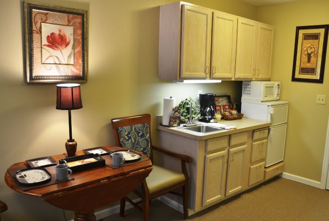 A cozy kitchenette with a small table and chairs, cabinets, and a lamp.