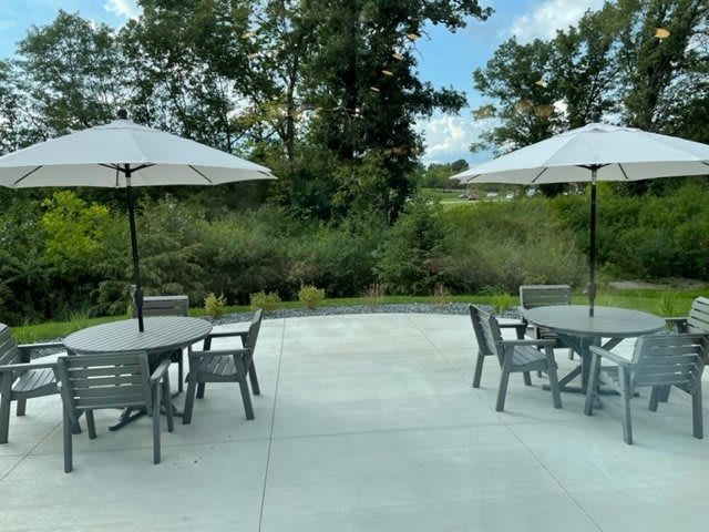A scenic outdoor patio area with tables and chairs under large umbrellas, surrounded by lush greenery.