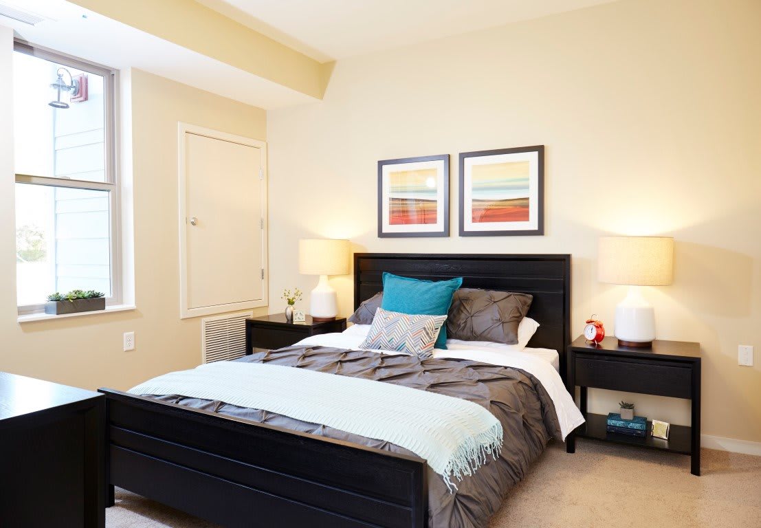 A modern bedroom with a neatly made bed, accented by colorful artwork and matching lamps on nightstands.