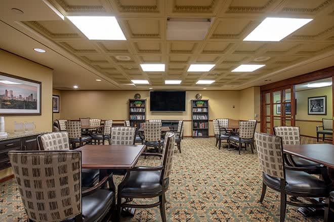A well-lit dining area featuring multiple tables and chairs, a television, and bookshelves.
