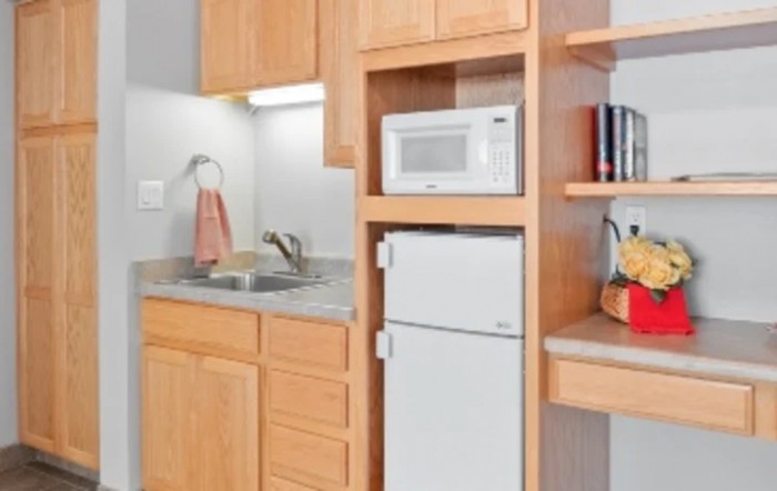 A compact kitchen area featuring a microwave, refrigerator, sink, and wooden cabinets.