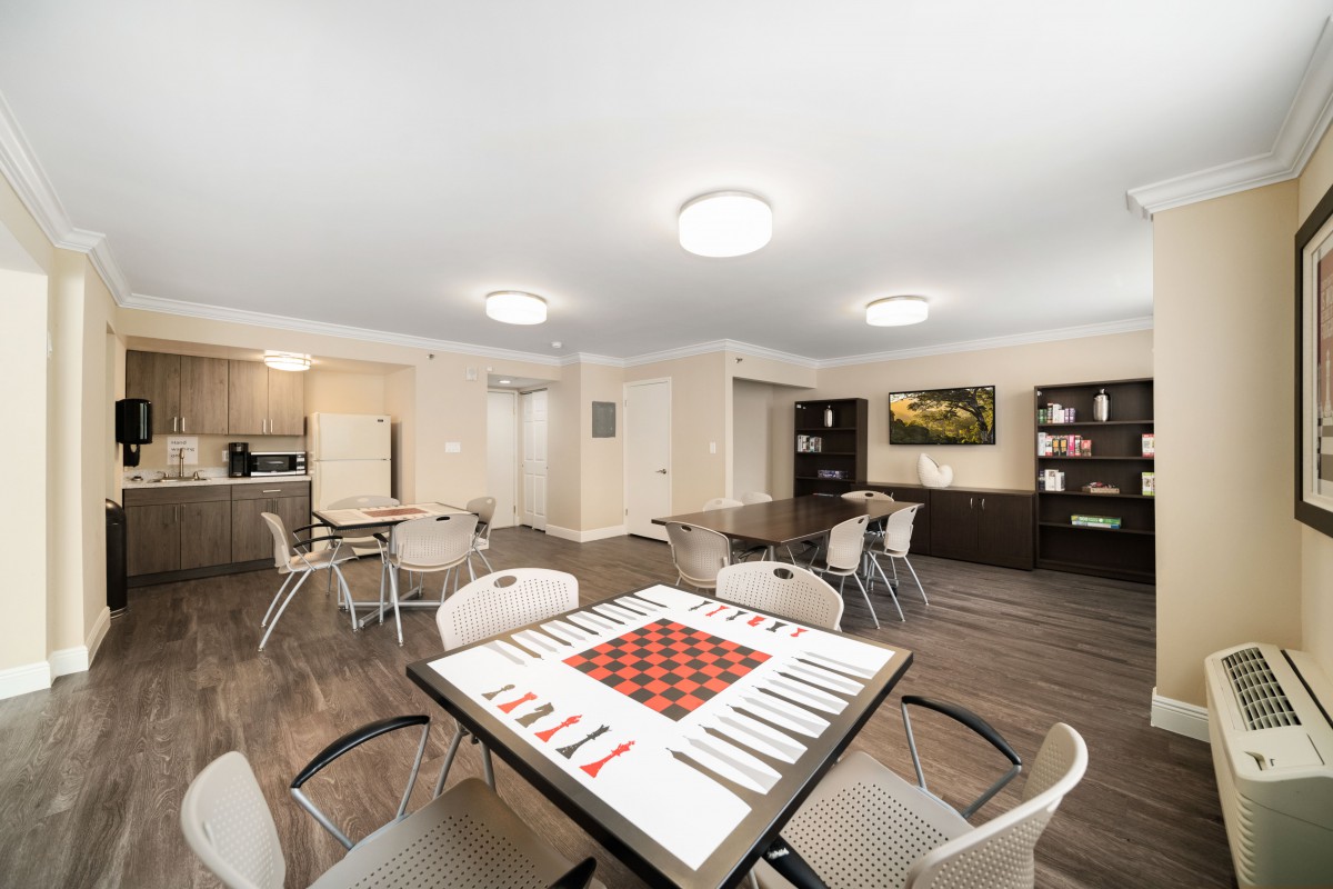 A modern living space featuring a chessboard on a table, surrounded by chairs with an adjacent kitchen area.
