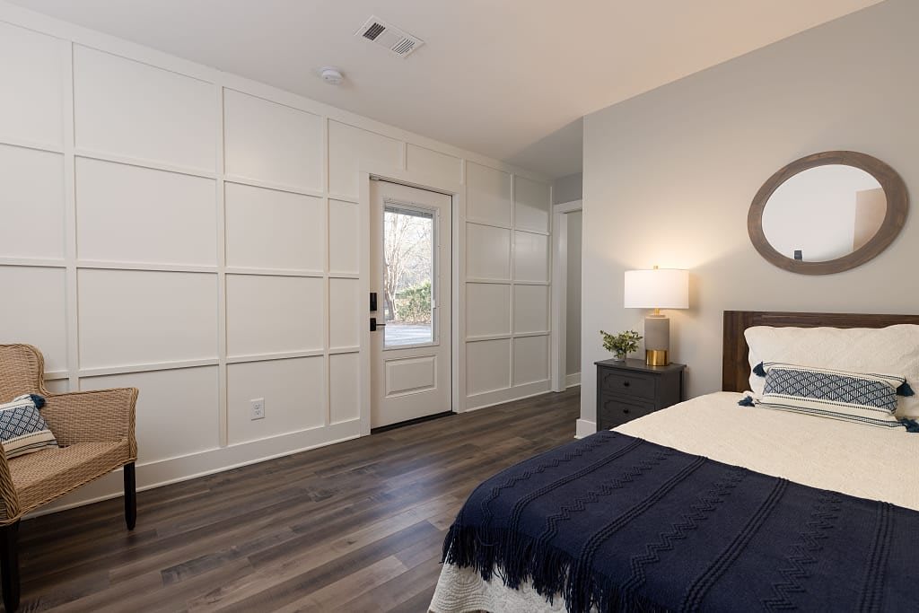 A contemporary bedroom with white paneled walls, dark wood flooring, and modern decor.