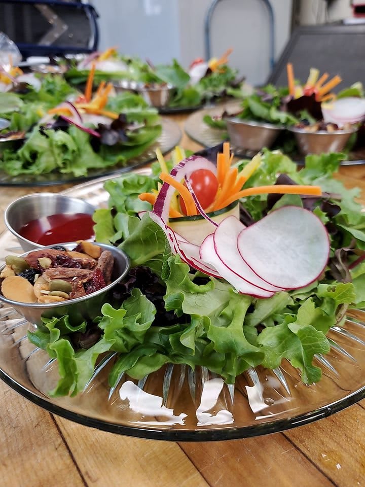 A fresh mixed green salad with radishes, carrots, and almonds served on a glass plate.