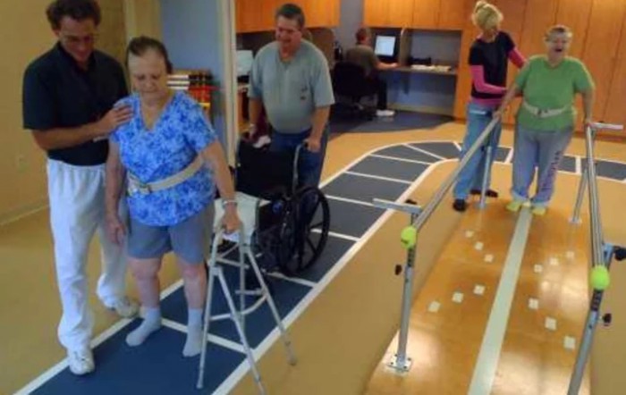 Elderly individuals engaged in a rehabilitation session using walkers and a support rail.