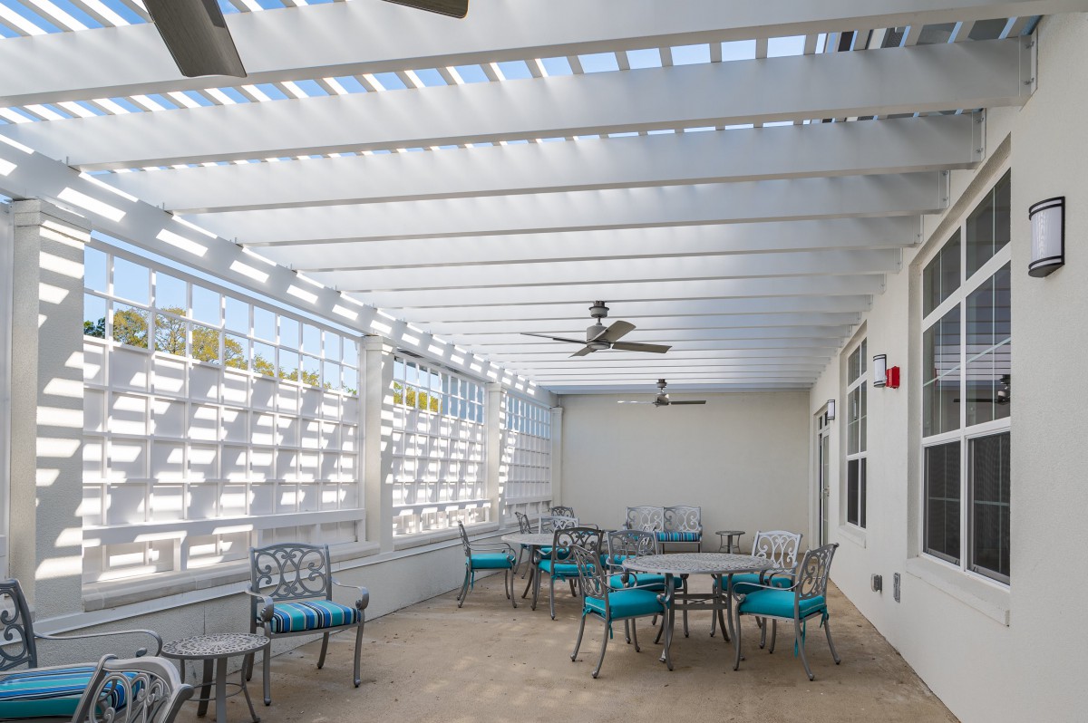 A modern outdoor patio with tables, chairs, and ceiling fans under a pergola.