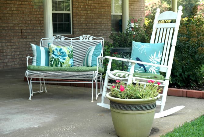 A porch with a rocking chair, cushioned bench, and a planter with flowers.