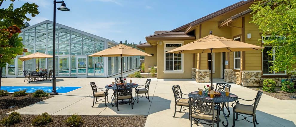 A sunny patio area with tables, chairs, and umbrellas next to a modern building.